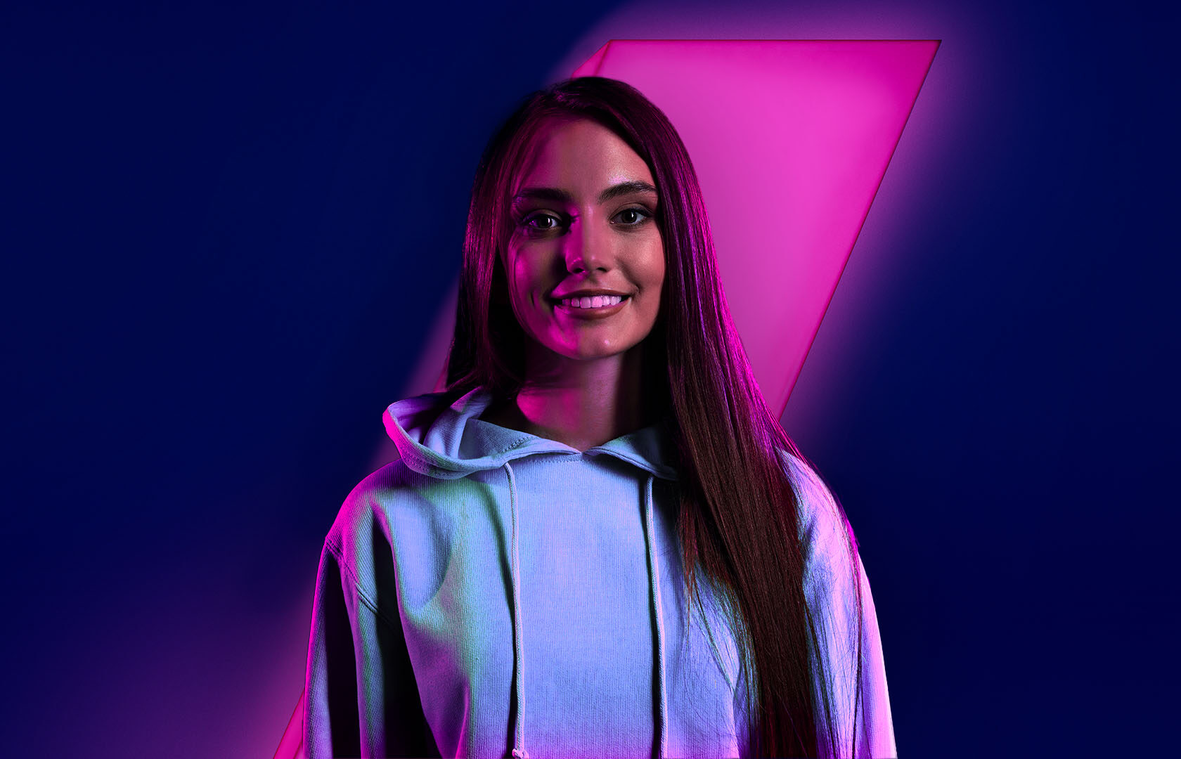 Vrouw kijkt in de camera. Achtergond met blauw en roze slash. Vacaturefoto CDD Analist Werken bij Welten.